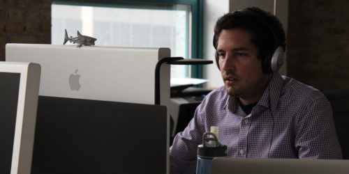 A man with headphones on working at his computer screen