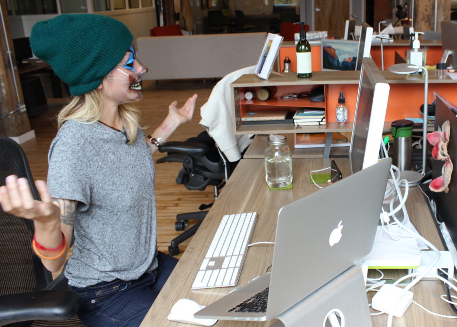 A woman in a Halloween clown mask shrugging frustratedly at a computer.