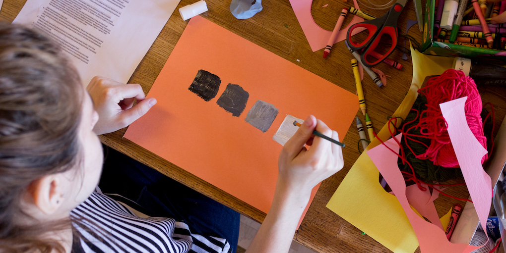 Woman painting black to white gradient squares on an orange sheet of paper
