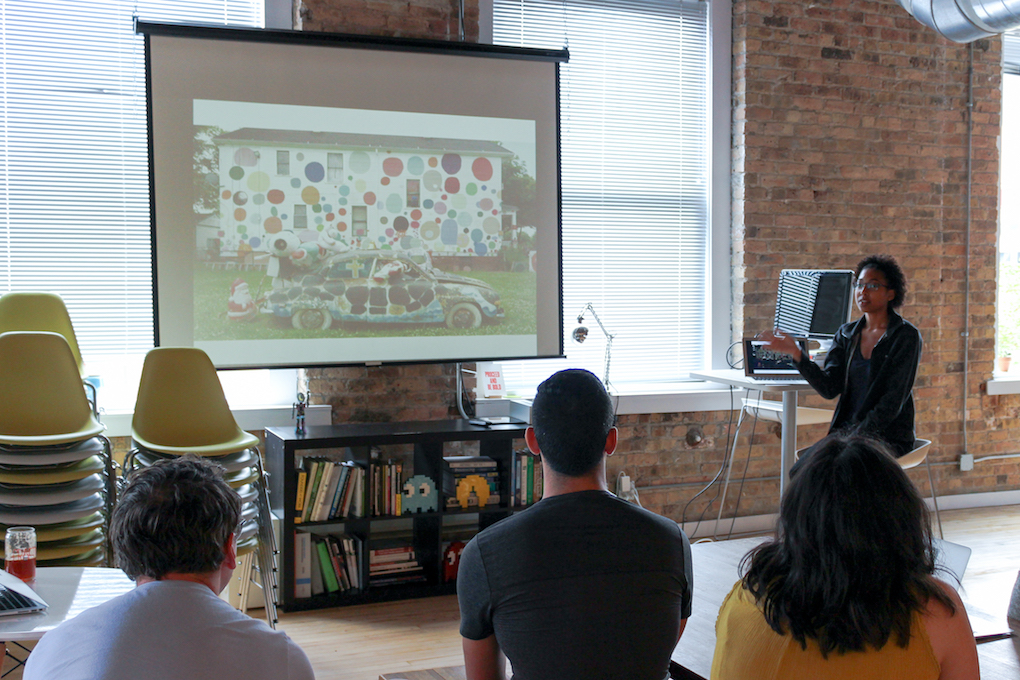 A woman presenting a Powerpoint presentation on a projected screen in front of an audience