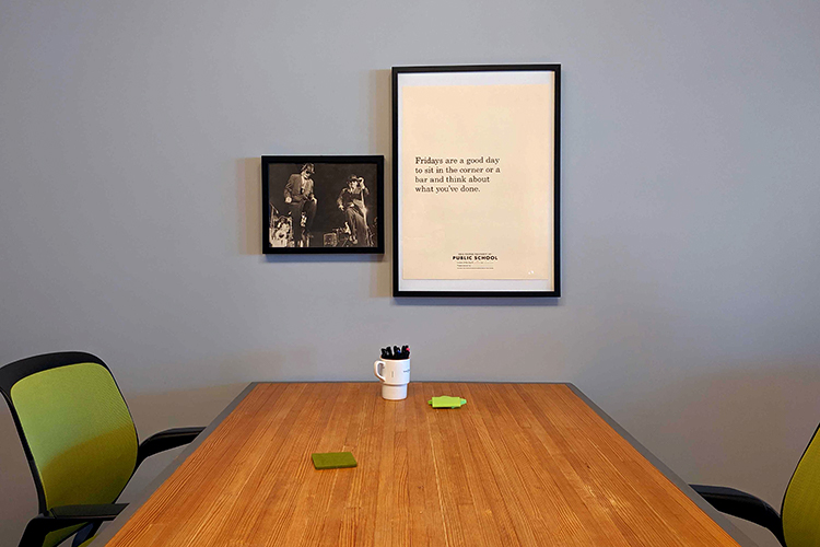 A large, plain poster that reads "Fridays are a good day to sit in the corner or a bar and think about what you've done," and a black and white photo of the blues brothers hang above a wooden table.