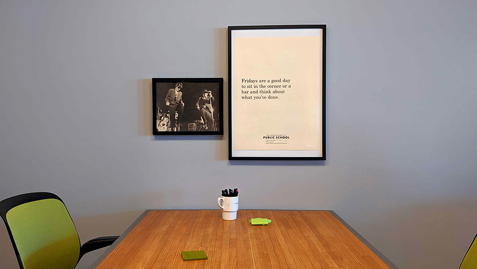 A large, plain poster that reads "Fridays are a good day to sit in the corner or a bar and think about what you've done," and a black and white photo of the blues brothers hang above a wooden table.