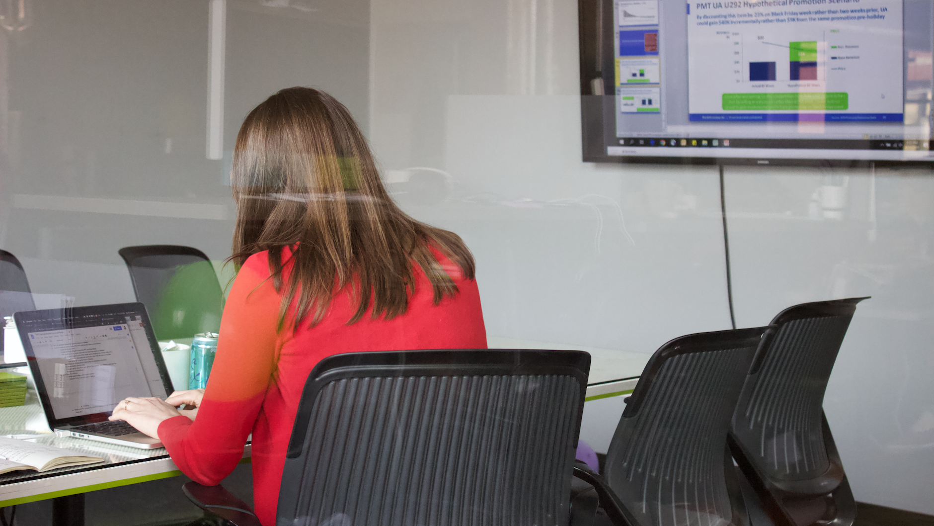 A designer sits at a conference room table, ready for a remote meeting in Zoom