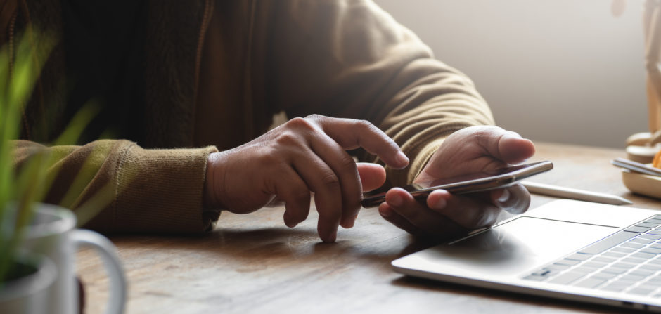 Cropped shot of person using their smartphone while working on his project in comfortable office room