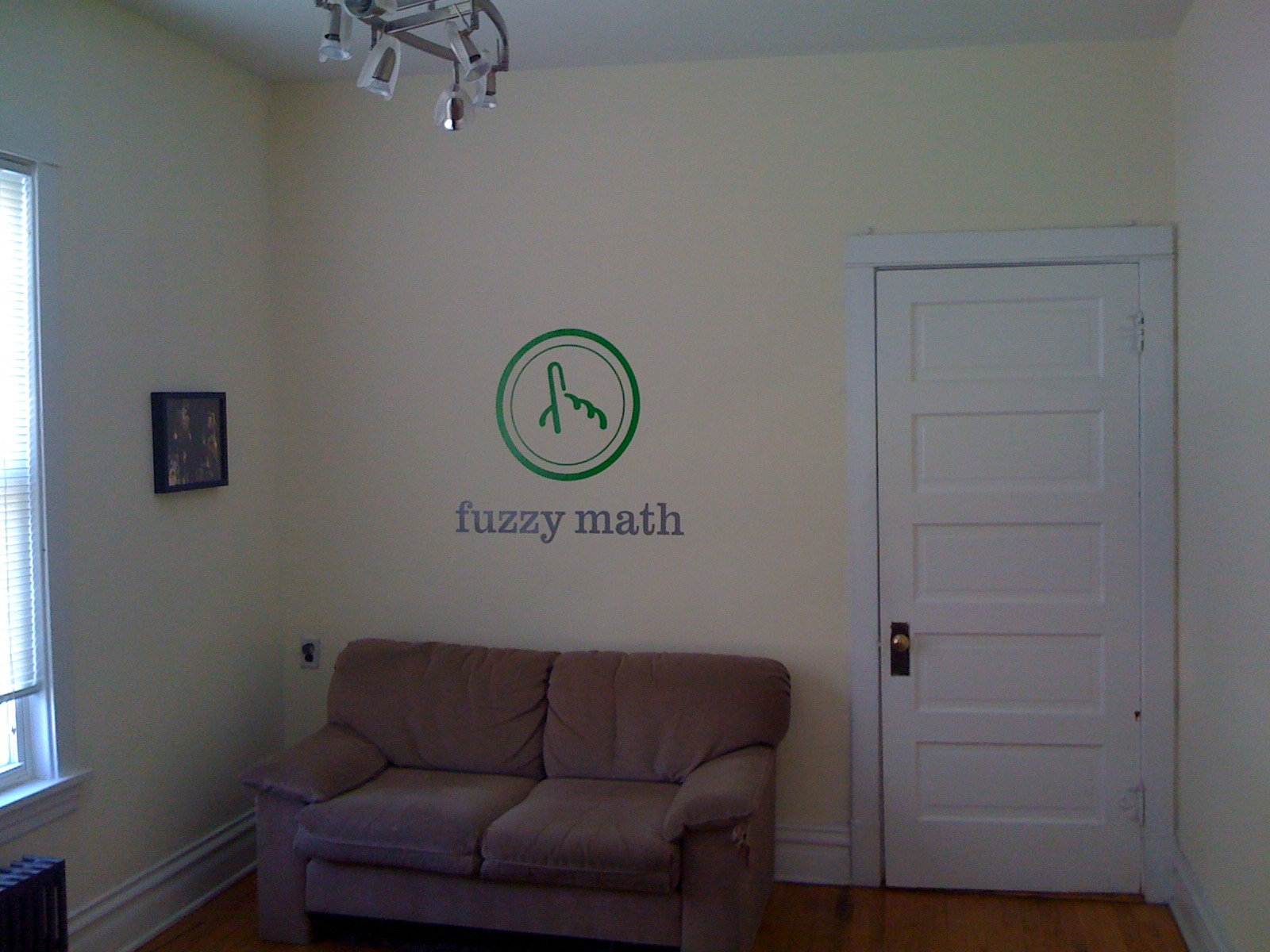 A small room with a couch, window, door, and Fuzzy Math logo on the wall.