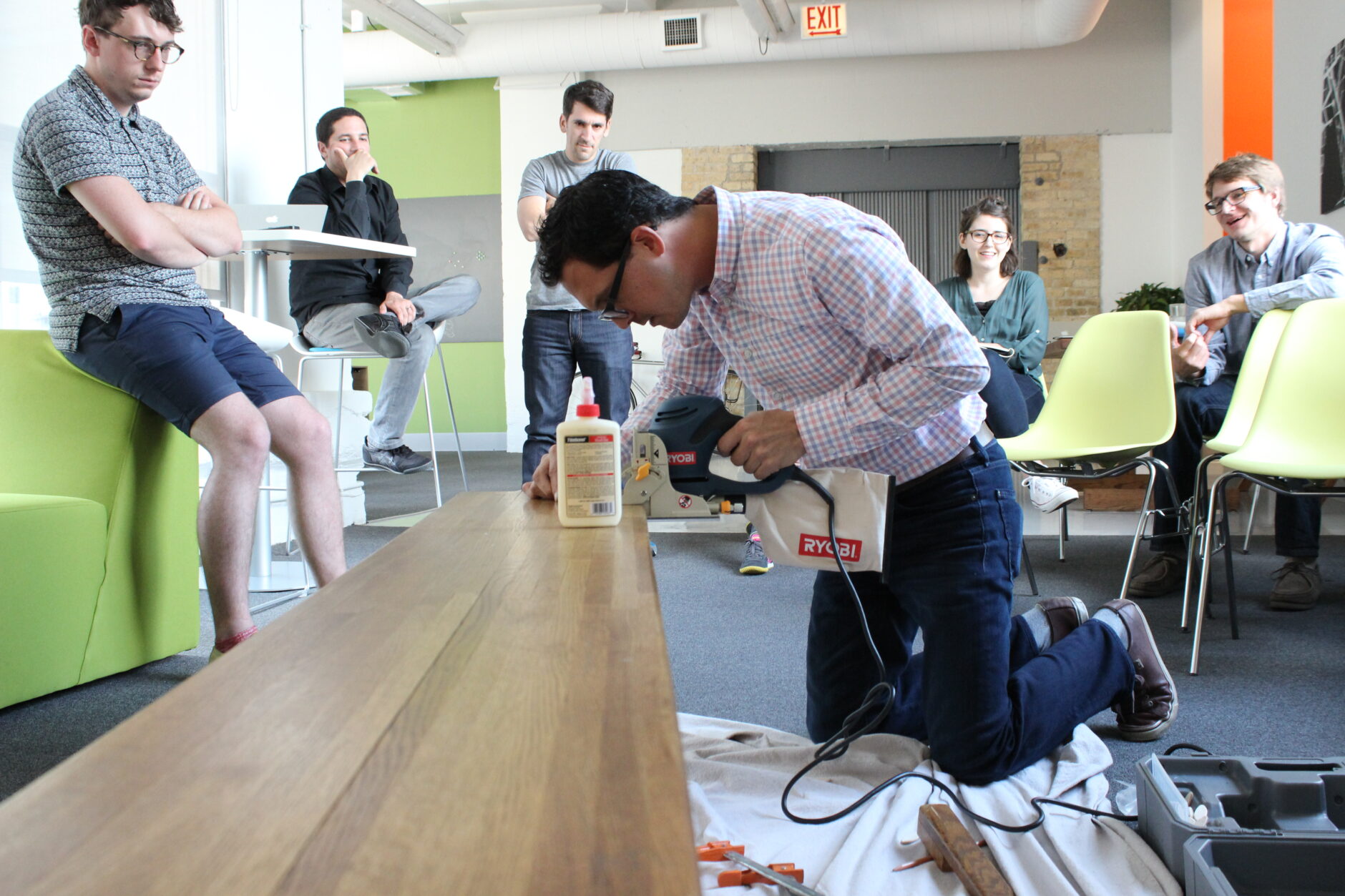 Mark building a bench during a skill share activity surrounded by co-workers watching in amusement.