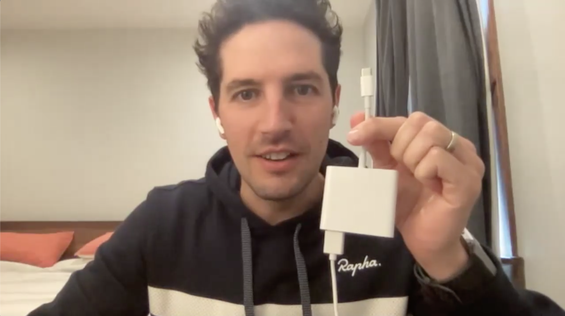 A white man with brown hair is wearing a hoodie and is holding up a large, clunky, Macbook USB-C dongle with a USB cord plugged into the back. He looks amused, but also kind of annoyed.
