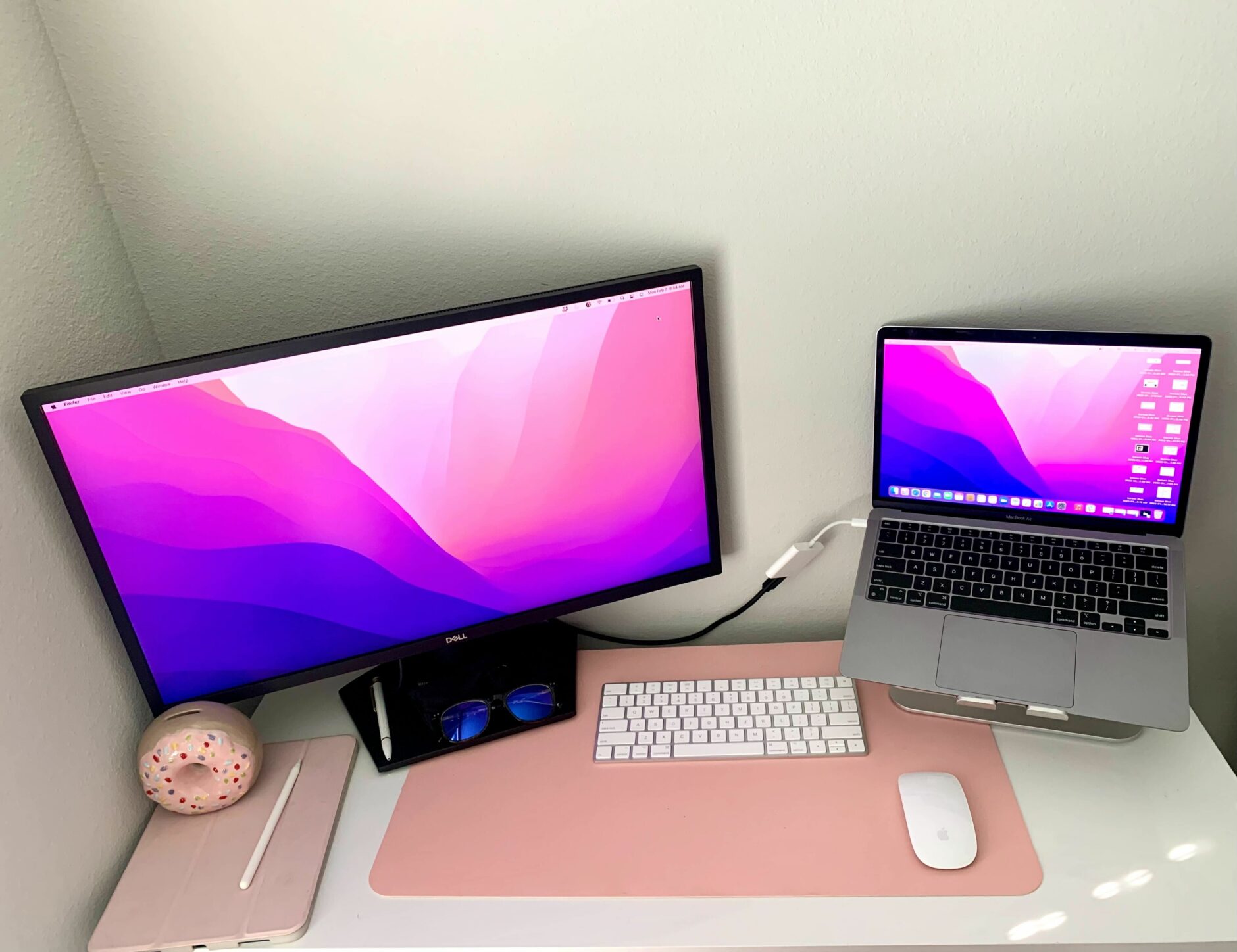 Brittany's desk setup which includes a monitor and laptop with a pink desk pad underneath. 