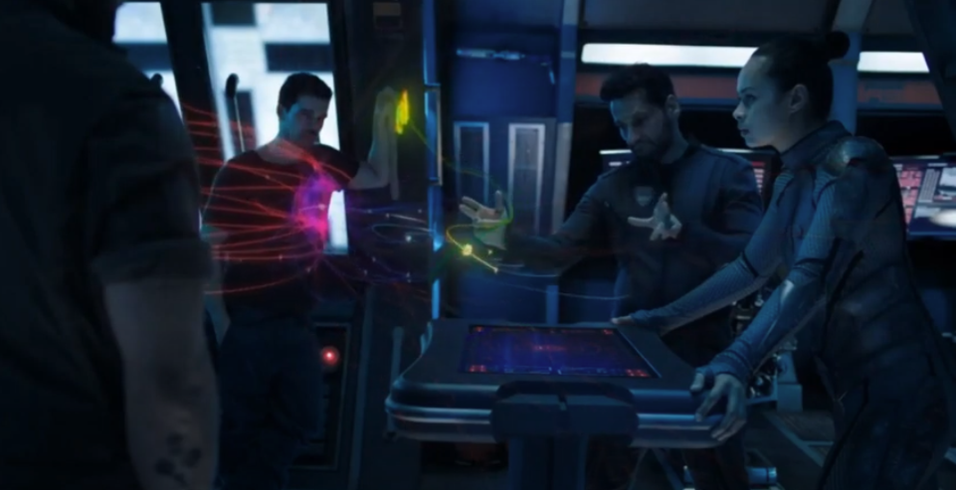 Four crew members aboard the Rocinante interacting with a holographic user interface on the center console of the ship.