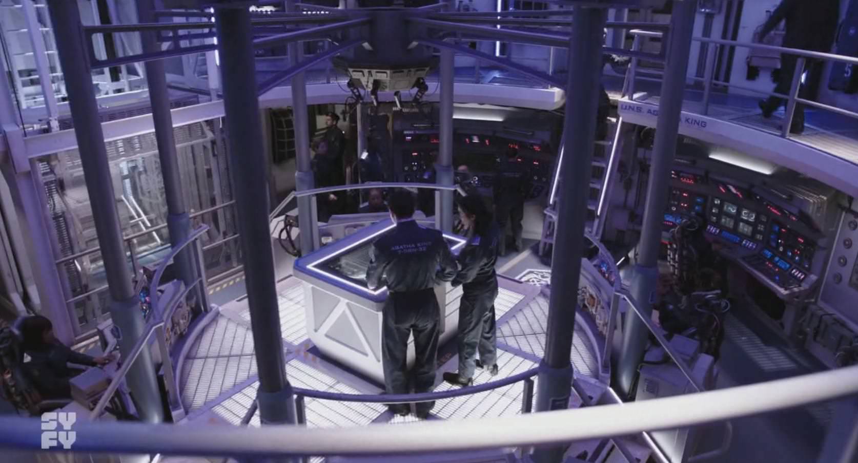 Bridge of the Agatha King showing 2 crew members huddled around the center control console.