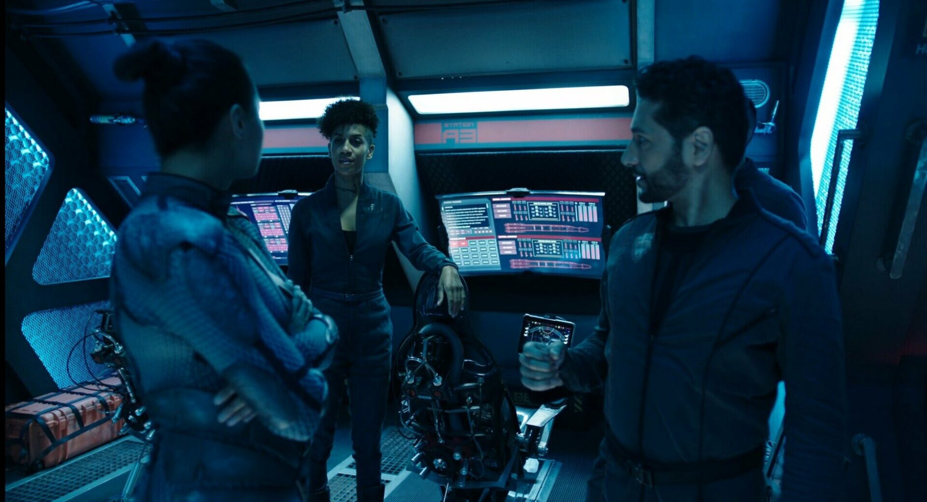 Three Rocinante crew members talking on desk with curved panels behind them.